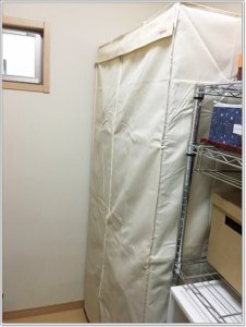 手持ちのラックにワードローブカバーをかけて服を埃（ほこり）から守る